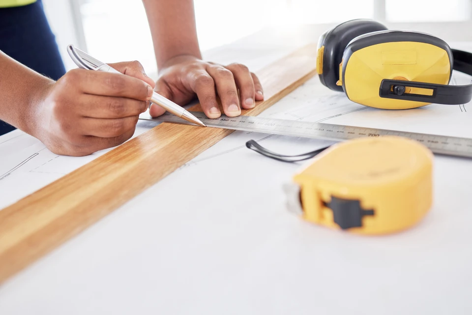 Professionnel de la rénovation en tenue de travail (casque ou gilet de chantier) supervisant et coordonnant des travaux de rénovation intérieure en cours sur un chantier, interagissant avec des outils ou des matériaux visibles (cloisons, carrelage, outils), incarnant le rôle d'interlocuteur unique qui gère l'ensemble des aspects du projet de rénovation.